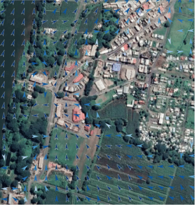 Aerial view of a town with buildings and fields. Blue arrows overlayed on the image indicate wind flow direction.