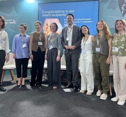 A group of seven people stands together indoors in front of a sign congratulating flood protection award 2025 recipients. They are smiling and wearing conference badges.