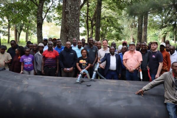 A group of people stand outdoors around a large black inflatable structure, posing for a photo among trees.